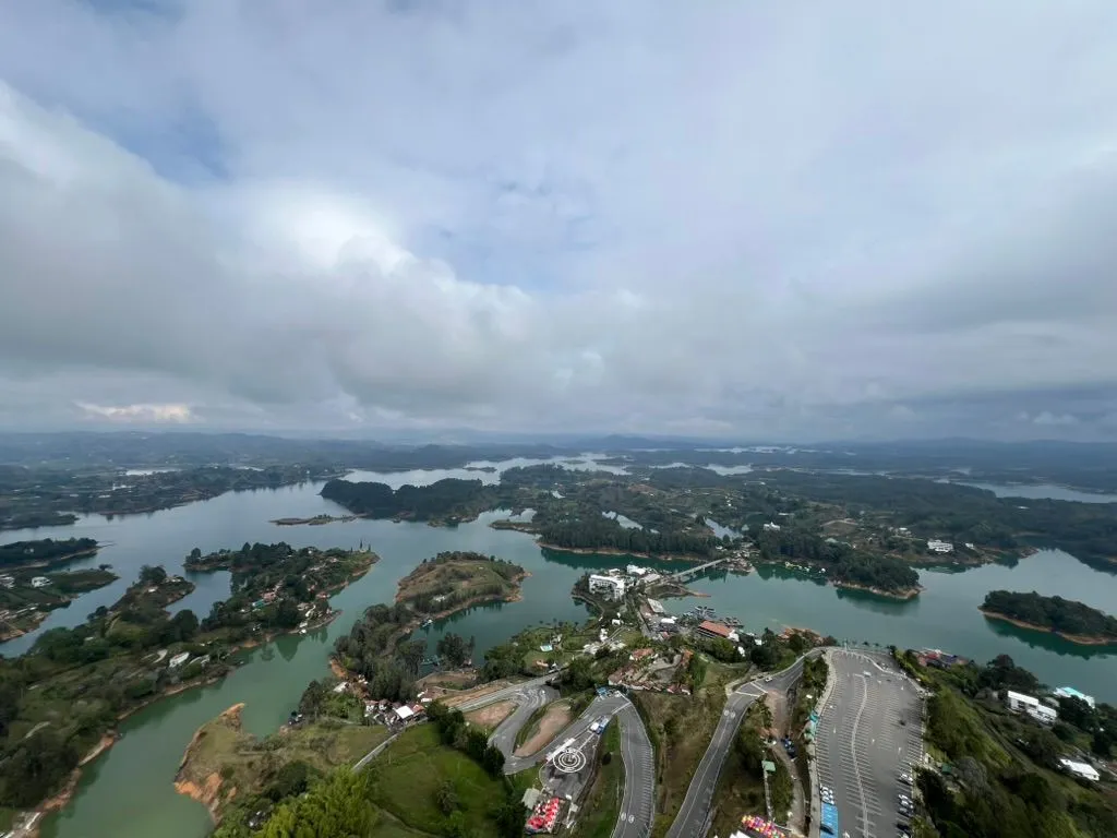 A green reservoir full of forested islands seen from far above, with switchback roads and a car park below